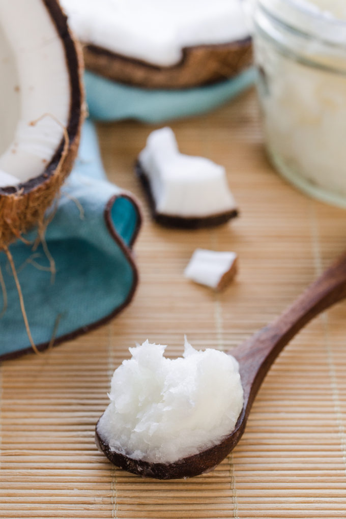 A scoop of coconut oil on a bamboo mat with fresh coconut pieces in the background.