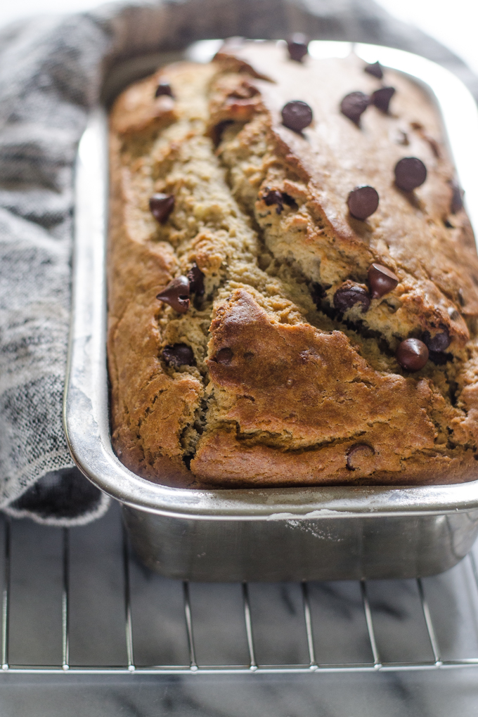 Sourdough banana bread in loaf pan on a cooling rack on a marble surface.