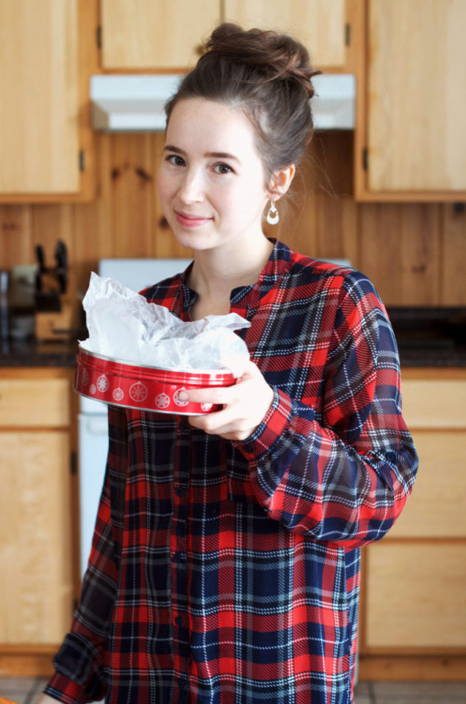 Woman in a plaid shirt holding a Christmas tin.