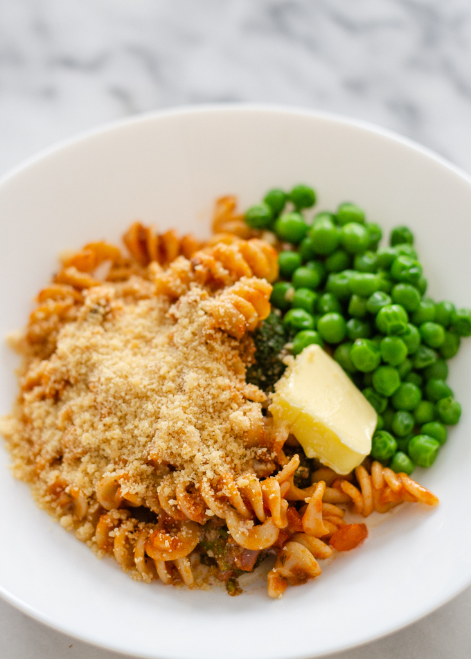 Leftover spaghetti and green peas in a bowl topped with butter and parmesan cheese.