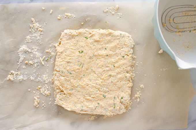 The cheddar biscuits dough patted out to a rectangle on a piece of parchment paper.