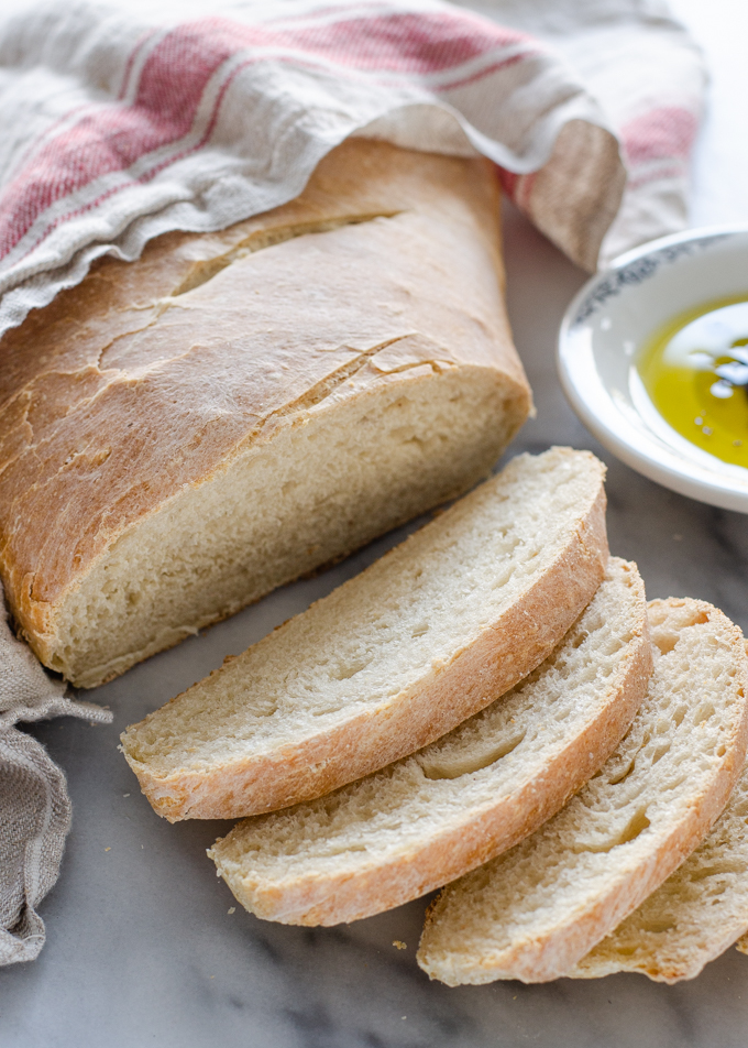 A sliced loaf of Soft Sourdough French Bread No Yeast all baked with a dish of olive oil and vinegar in the background.