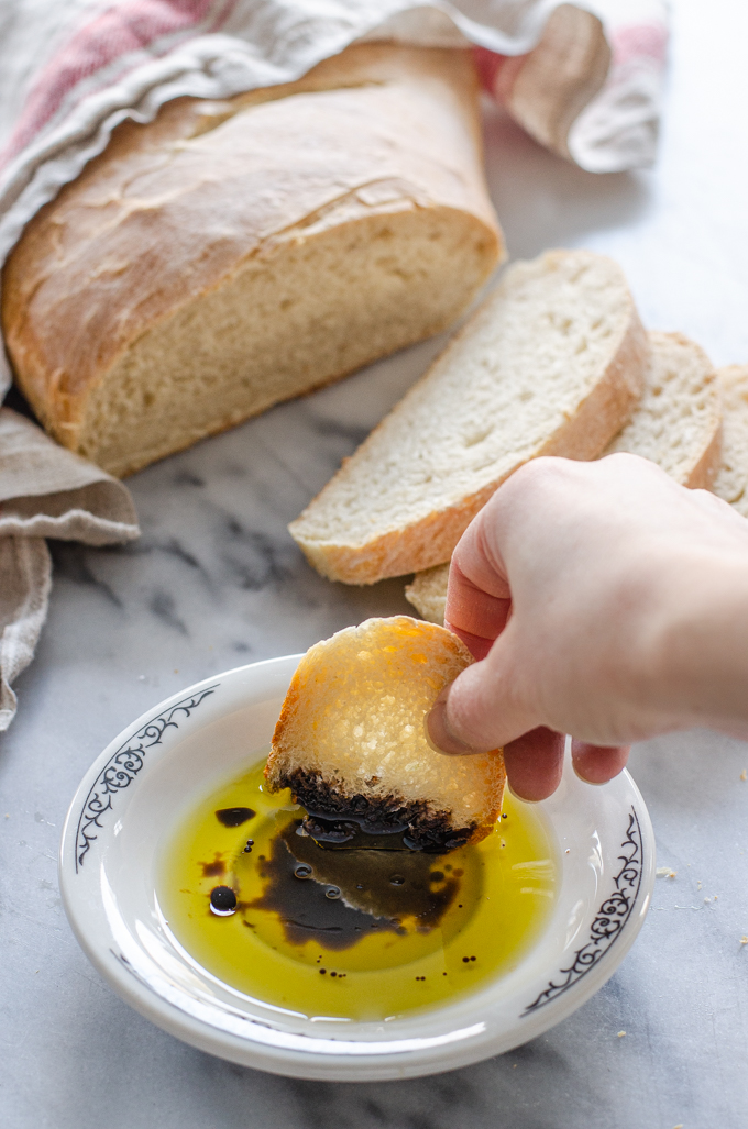 Dipping a slice of soft sourdough bread into a dish of olive oil and balsamic vinegar.