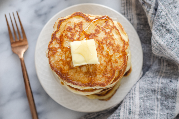 A stack of sourdough pancakes with a pat of butter and drizzle of maple syrup on top.
