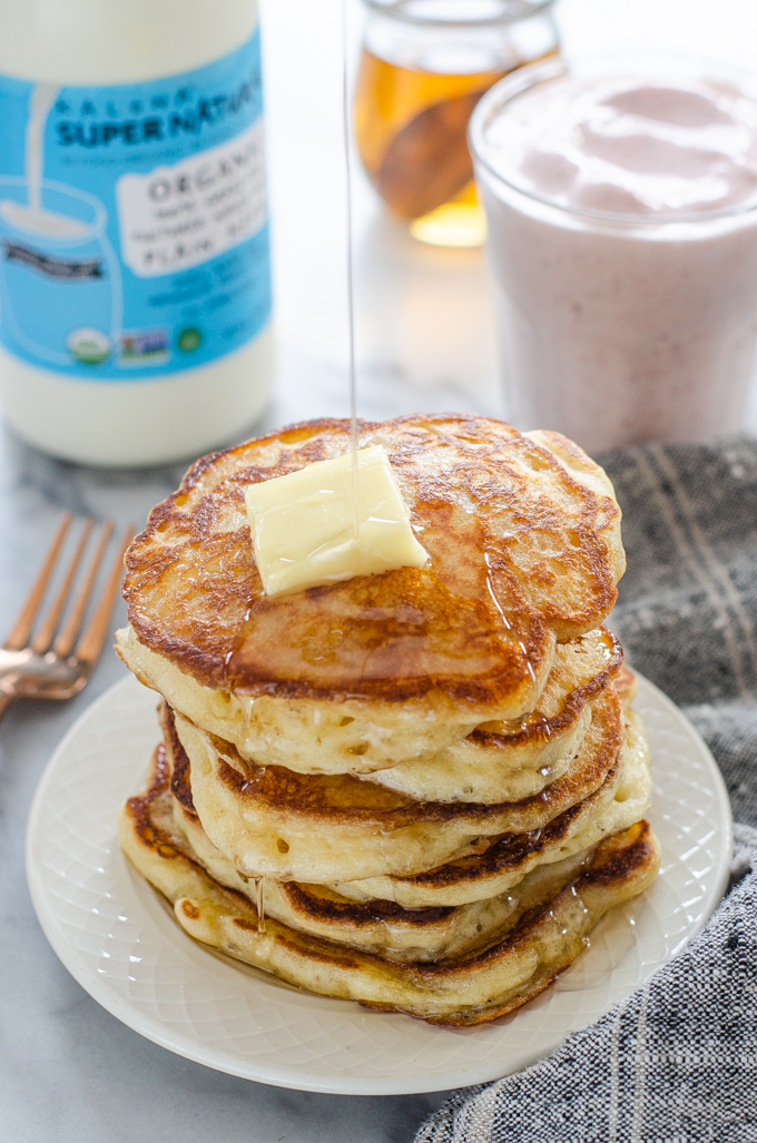 Drizzling maple syrup onto a stack of sourdough pancakes.