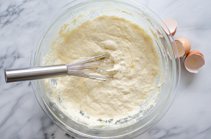 The bowl of batter on a marble surface with a whisk in it.