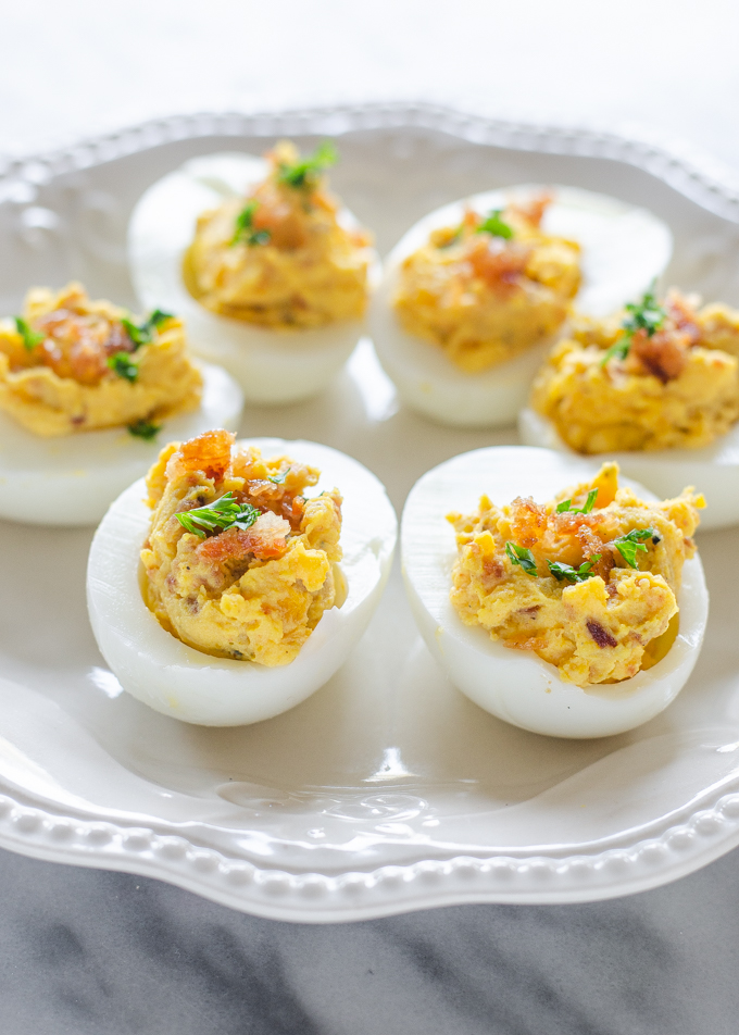 Deviled eggs with bacon and garnished with parsley on a pretty plate.