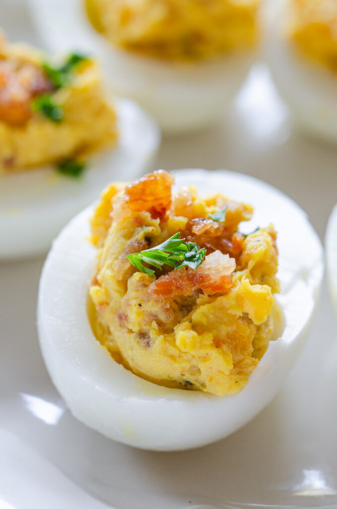 A close up shot of deviled eggs with bacon garnished with parsley. 