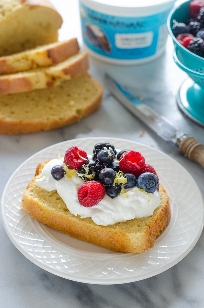 A slice of sour cream pound cake loaf topped with whipped cream and berries.