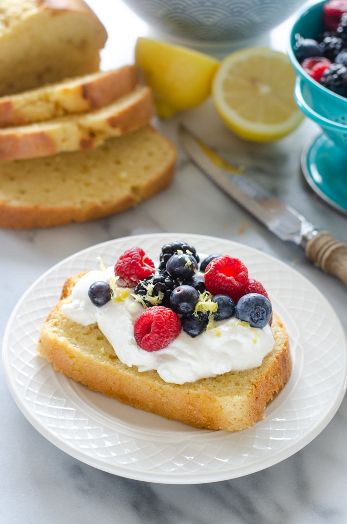 A slice of sour cream pound cake loaf topped with whipped cream and berries.