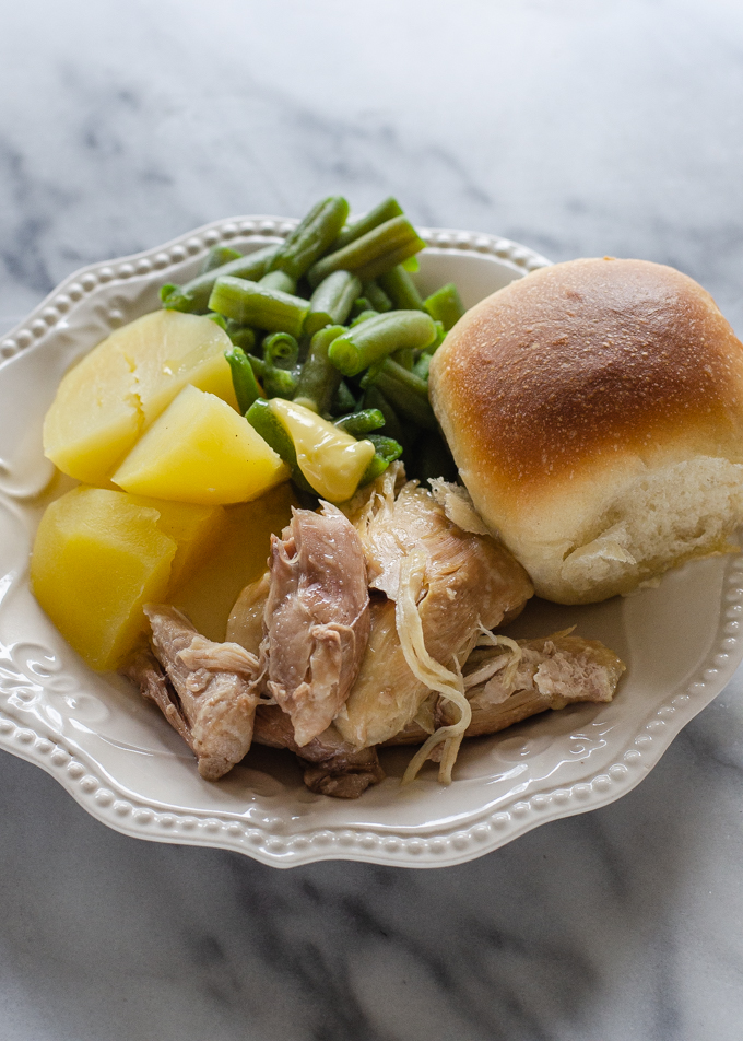 A plate filled with Instant Pot chicken, boiled yukon gold potatoes, green beans, and a sourdough roll.