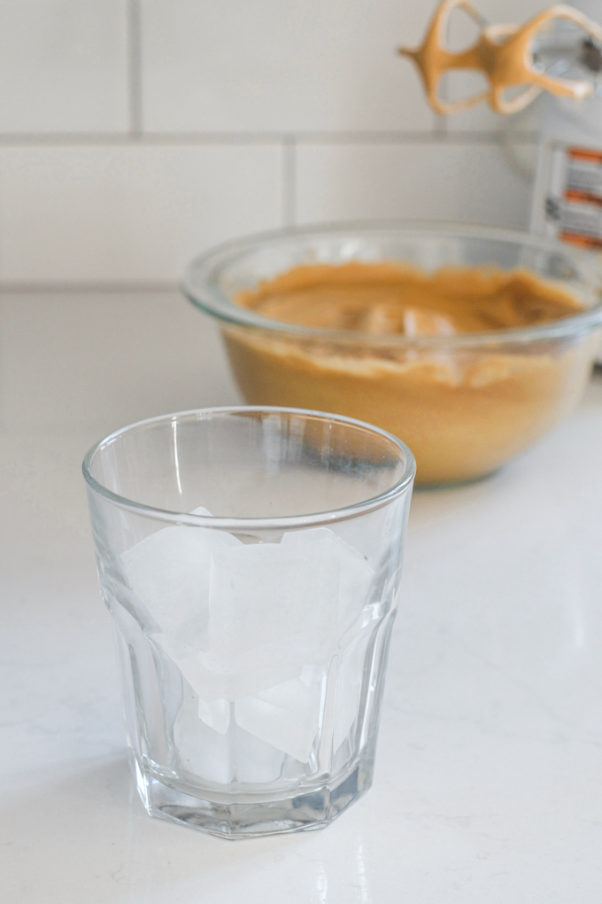 Ice cubes in a glass with the whipped coffee in the background.