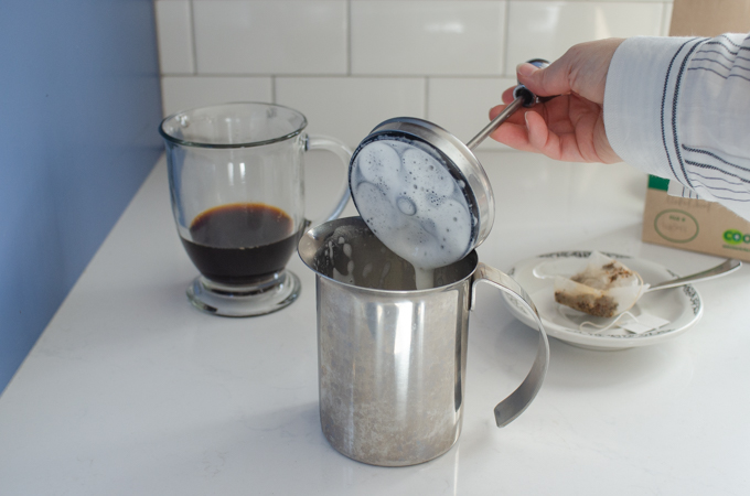 Lifting the lid off of the hand pump milk frother.