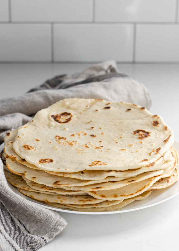 Sourdough tortillas stacked on a plate with a tea towel around them.