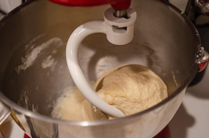 The kneaded dough in the bowl of a stand mixer with the dough hook still attached.