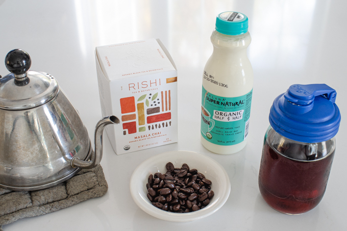 All of the ingredients to make a dirty chai latte laid out on a white countertop.