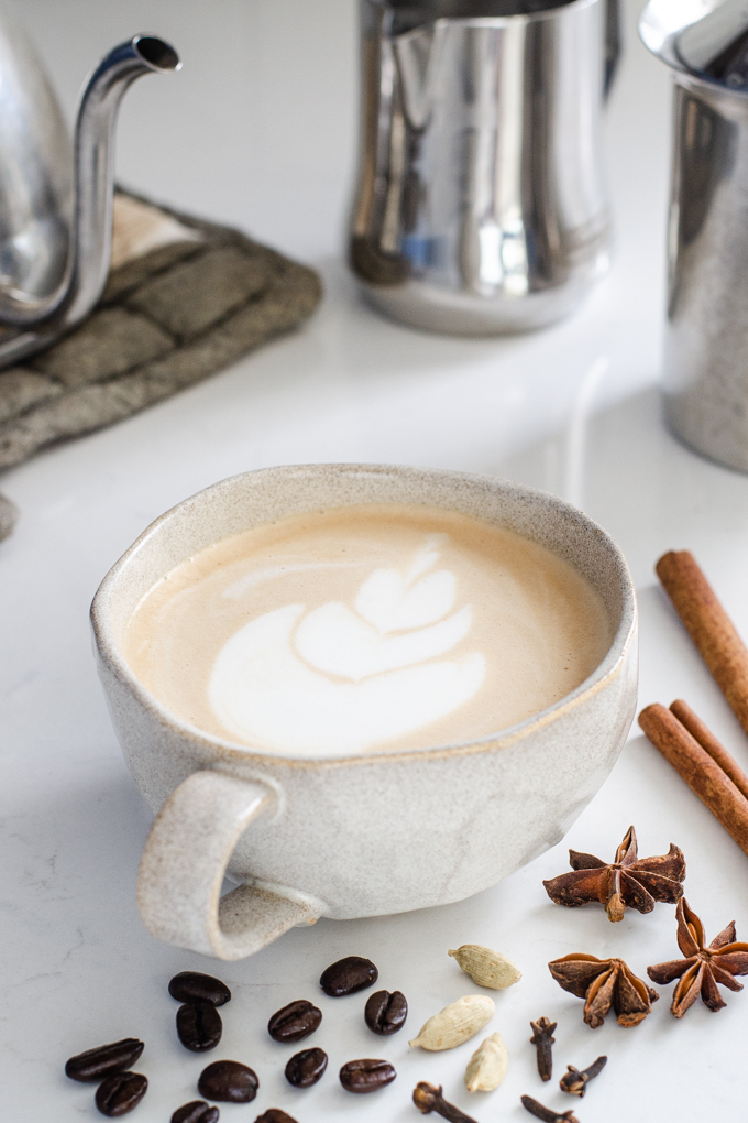 A mug of dirty chai latte with spices around it.