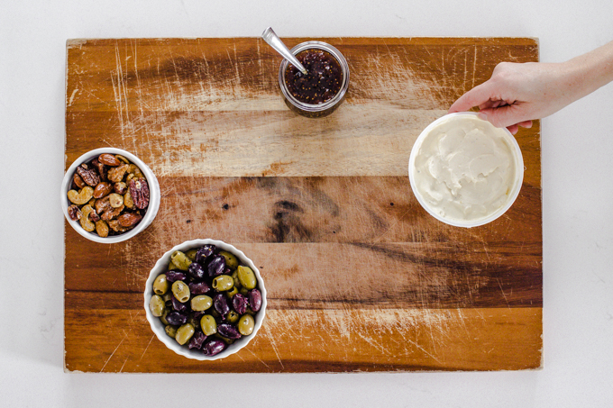 Arranging containers of snacks on a wooden cutting board.