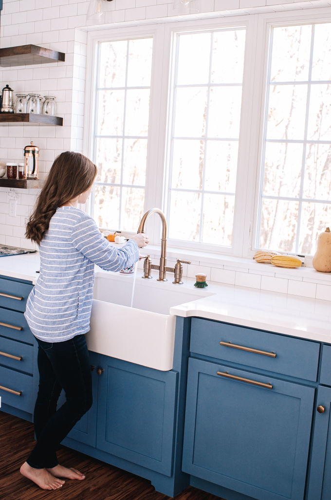 Blue transitional cabinets with white quartz countertops and a white apron front sink in front of window.