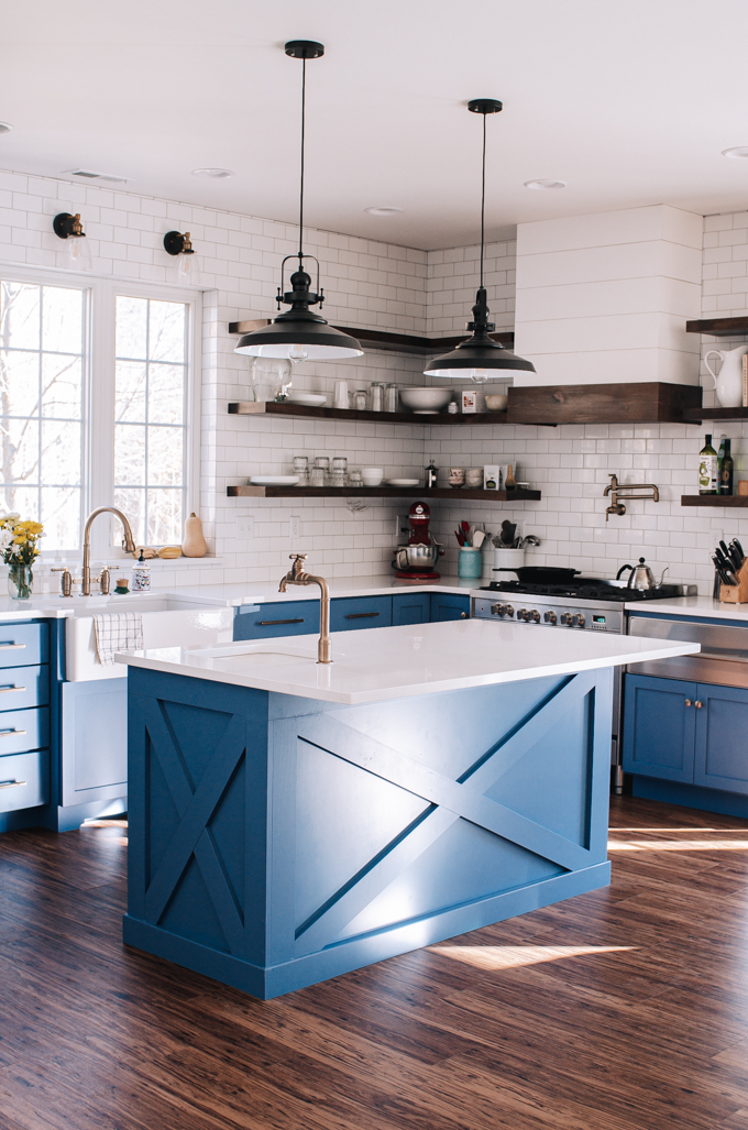 Transitional industrial farmhouse style kitchen with blue cabinets, subway tile backsplash, white quartz counters, and open shelving.