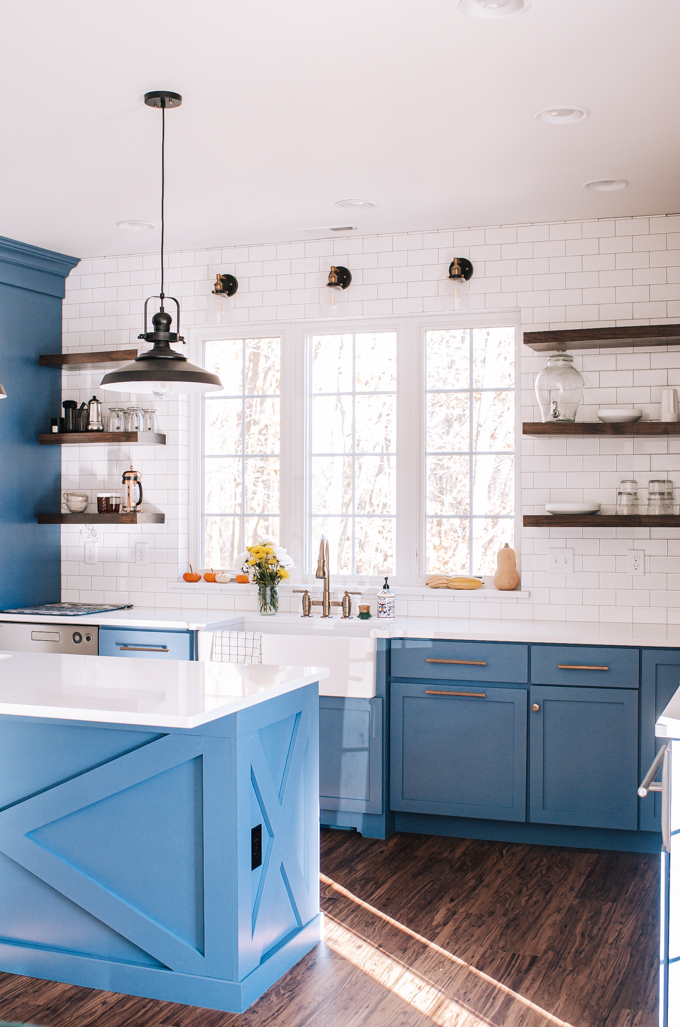 Transitional industrial farmhouse style kitchen with blue cabinets, subway tile backsplash, white quartz counters, and open shelving.