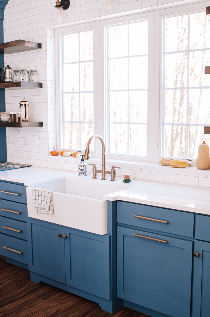 White apron front sink with a pull out bridge faucet in front of windows.