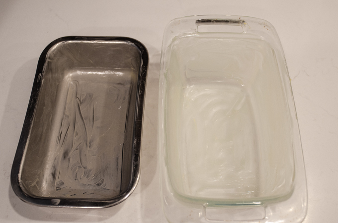 Greasing two loaf pans: one stainless steel, and the other glass.