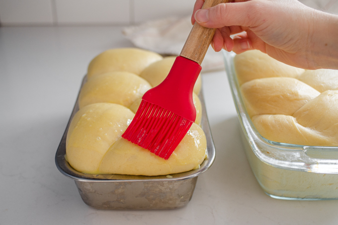 Brushing the top of the bun loaf with the egg wash.