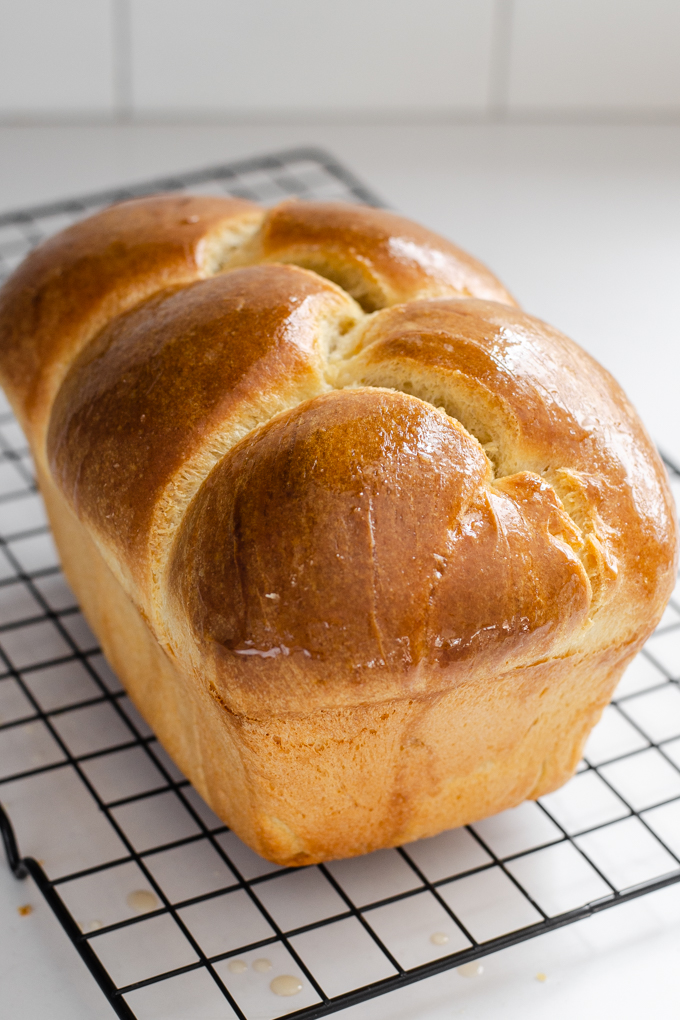 A loaf of sourdough brioche bread on a black wire cooling rack.