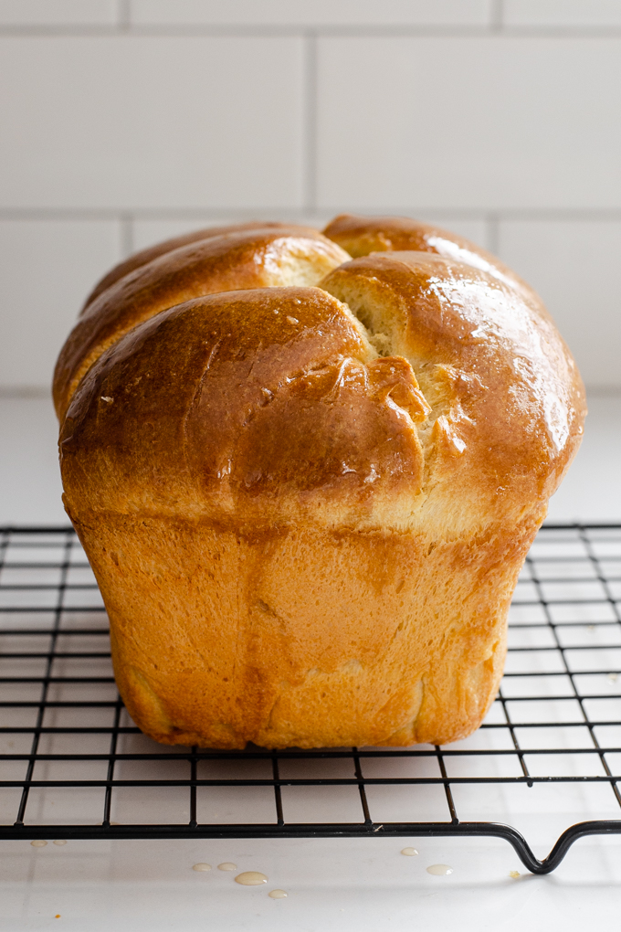 A loaf of sourdough brioche bread on a black wire cooling rack.