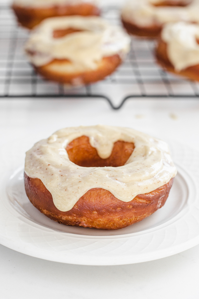 A sourdough donut on a plate with more doughnuts behind it on a wire cooling rack.