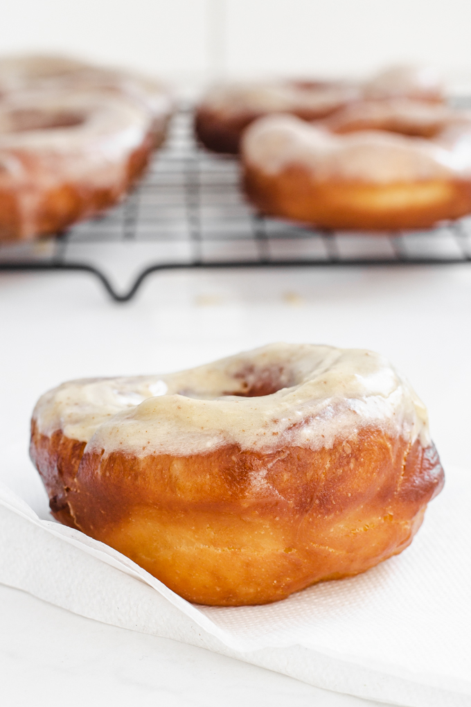 A donut on a napkin with more sourdough donuts on a wire cooling rack in the background.