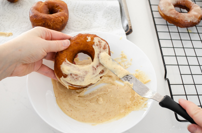 Spreading a doughnut with browned butter frosting.