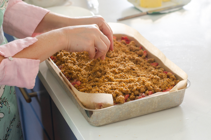 Adding the crumb mixture on top of the strawberry rhubarb filling and cake.
